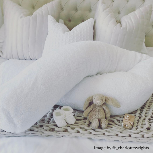 White pregnancy pillow on a bed with baby toys and booties